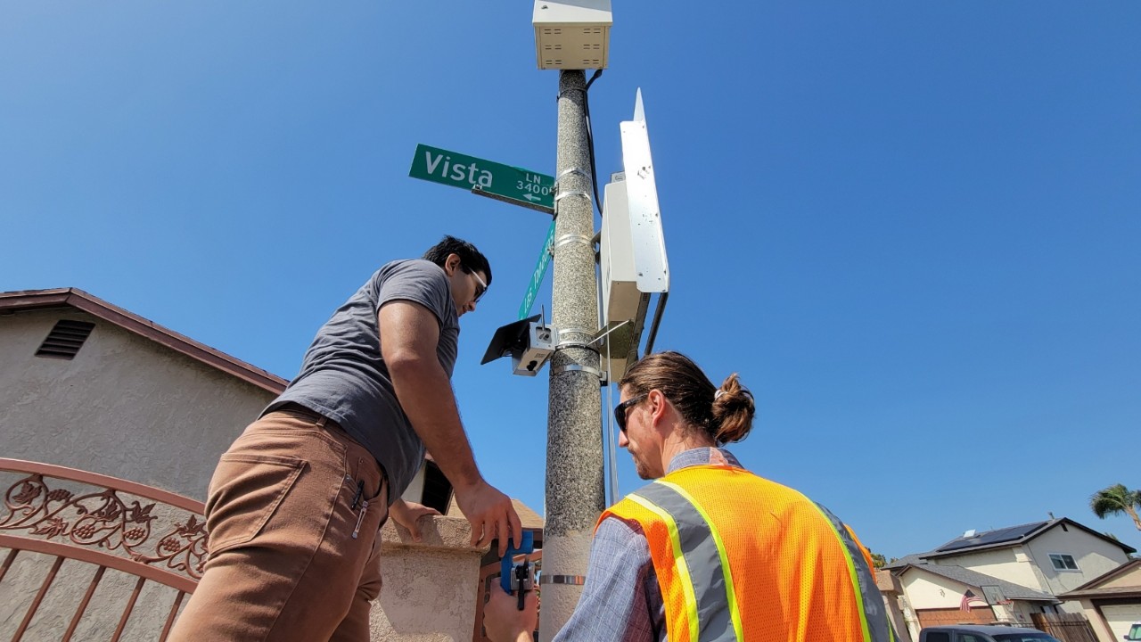 Two people install an air quality monitor. 