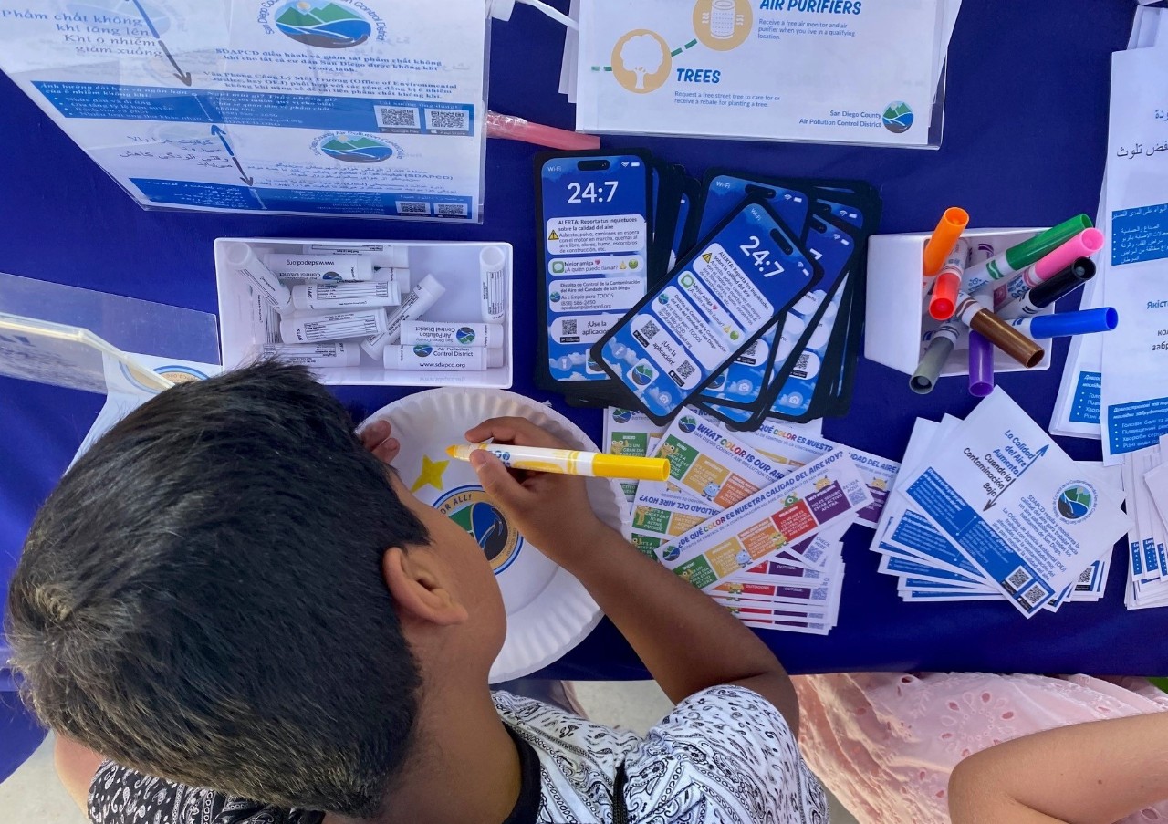 Picture of outreach table where child draws amid various SDAPCD resources.